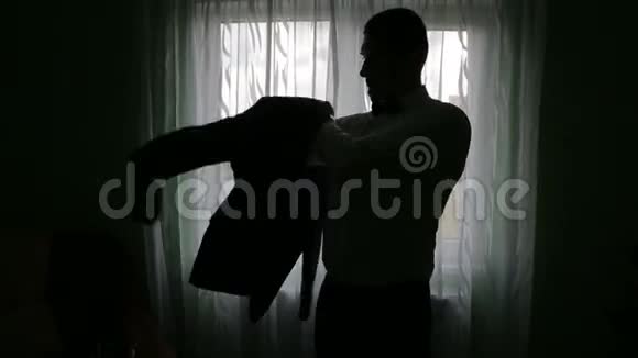 一个男人在黑暗的房间里穿上夹克的剪影视频的预览图