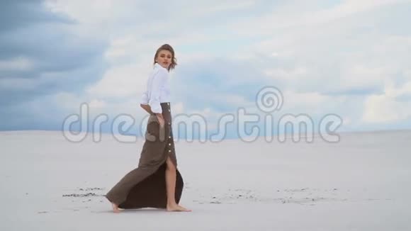 一个穿裙子和上衣的女孩沿着沙漠散步视频的预览图