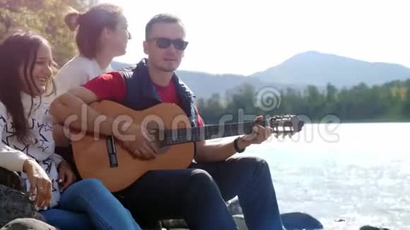 一群欢快的朋友在海边玩吉他唱歌在山河旁边的一个夏天3840x2160视频的预览图