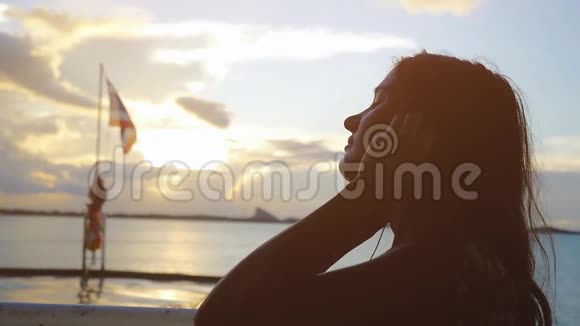 美丽梦幻的年轻女子带着耳机在航行中慢悠悠地听着音乐视频的预览图