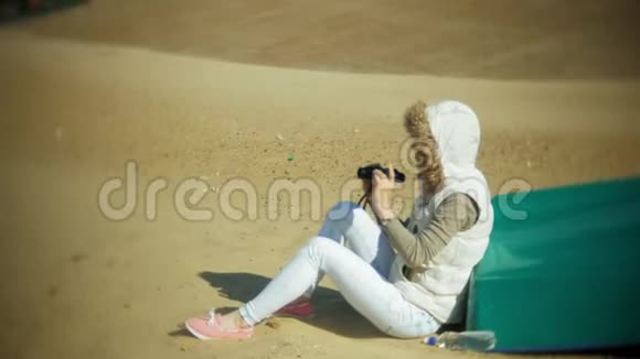 年轻女子坐在船外的海滩上用望远镜看着视频的预览图