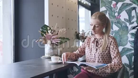 年轻的女学生在咖啡馆里学英语一个漂亮的金发女郎翻着杂志喝着咖啡视频的预览图