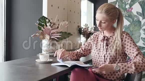 年轻的女学生在咖啡馆里学英语一个漂亮的金发女郎翻着杂志喝着咖啡视频的预览图