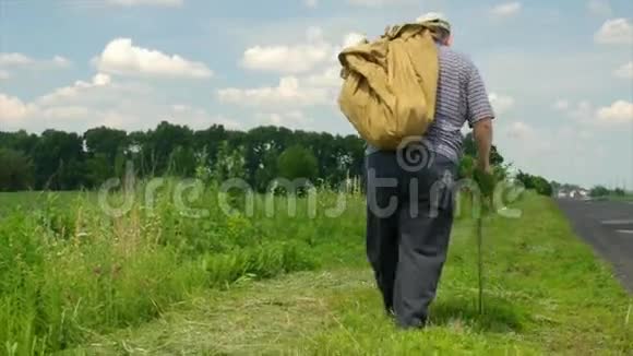 夏天一个带着手杖的老人背着一个沉重的袋子在路边移动视频的预览图