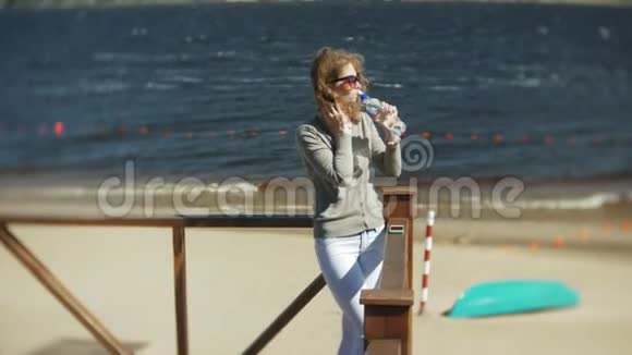 女人从海滩上的瓶子里喝水视频的预览图