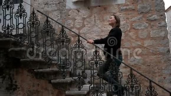 穿着破牛仔裤的年轻女子从石屋里爬上了一个金属梯子视频的预览图