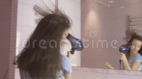 美丽快乐的女孩少年用吹风机吹干头发在浴室里的镜子前唱歌跳舞视频的预览图