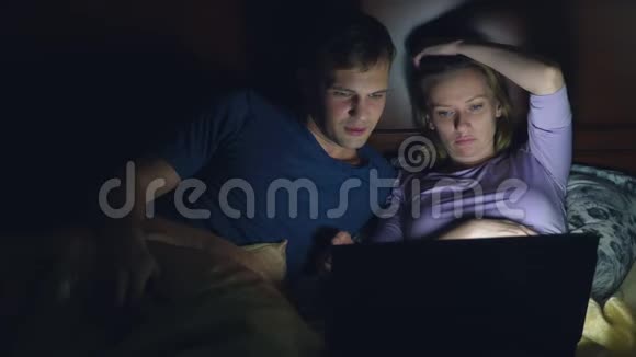 夫妻男人和女人在睡觉前在卧室的床上用笔记本电脑看电影看无聊的电影摔倒视频的预览图