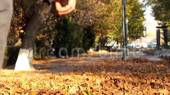 秋天雄性在橙色的落叶上行走男性用脚扔树叶离开摄像机视频的预览图