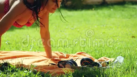 美丽的年轻女子戴着太阳镜躺在草地上听音乐用手机和唱歌3840x2160视频的预览图