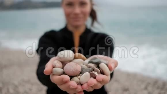 女人手里拿着一堆岩石在岸边与波浪视频的预览图