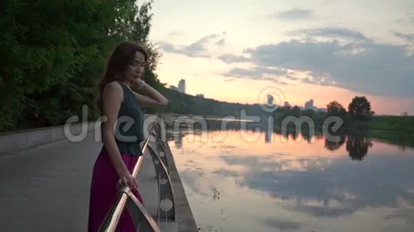 美丽的黑发女孩看着公园堤岸上的日落河慢镜头视频的预览图
