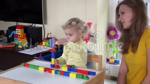女孩和妈妈在家里的小桌子旁玩彩色木砖视频的预览图