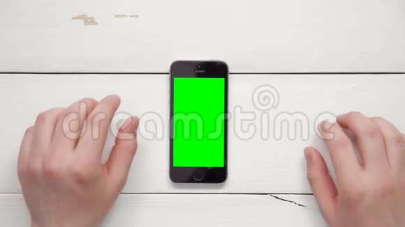从上面的复制空间可以看到男性双手在白色桌子上用绿色屏幕显示智能手机的多种手势视频的预览图