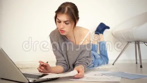 年轻漂亮的女士躺在地板上在家里用她的笔记本电脑工作视频的预览图