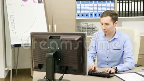 商人正在他办公室的电脑旁工作旁边是装满图表的文件夹视频的预览图