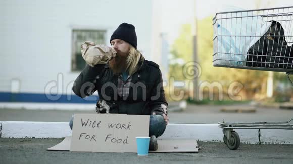 年轻人帮助无家可归的人给他一些食物而乞丐喝酒坐在购物车附近视频的预览图