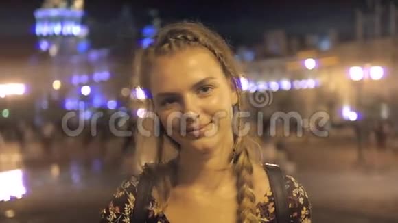 夜晚在城市街道上年轻漂亮的女子微笑着在灯光的背景下摆姿势视频的预览图