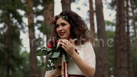 美丽的新娘穿着一件老式的连衣裙在夏天的森林里他头上戴着乌鸦的彩色鲜花视频的预览图