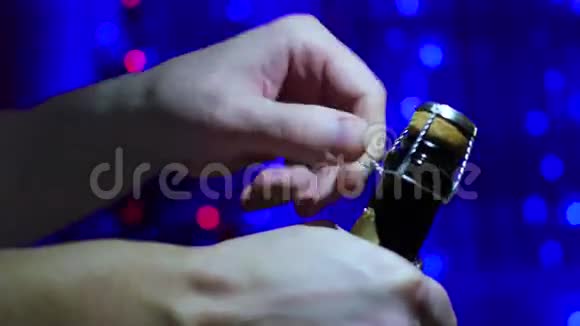 男子打开一瓶香槟特写背景中圣诞杉木的灯光和花环视频的预览图