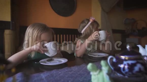 两个可爱的金发小女孩在舒适的现代咖啡馆喝茶视频的预览图