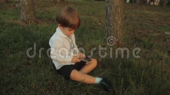 一个小男孩在公园里玩智能手机夏天日落夏天日落视频的预览图