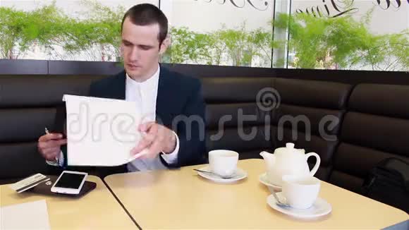 商人一边喝咖啡一边坐在咖啡馆里看文书工作视频的预览图
