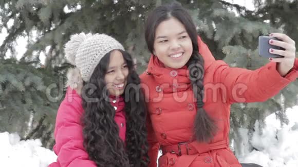 微笑的两个女孩自拍与智能手机户外温暖的衣服视频的预览图