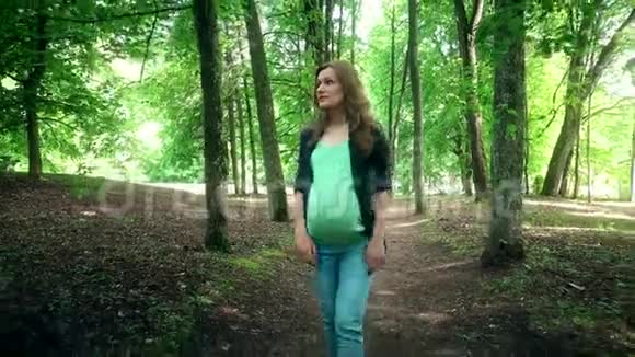 年轻的孕妇在树巷之间的夏日公园散步视频的预览图