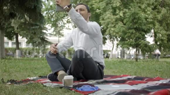 现代西班牙裔年轻人在公园里自拍带着他的平板电脑视频的预览图