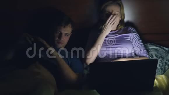 夫妻男人和女人在睡觉前在卧室的床上用笔记本电脑看电影看无聊的电影摔倒视频的预览图