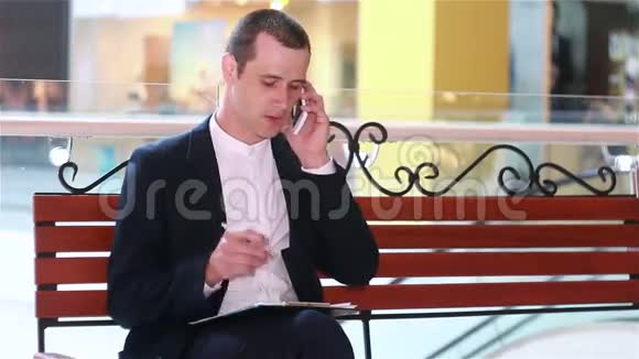 商人用智能手机说话在笔记本上写字视频的预览图