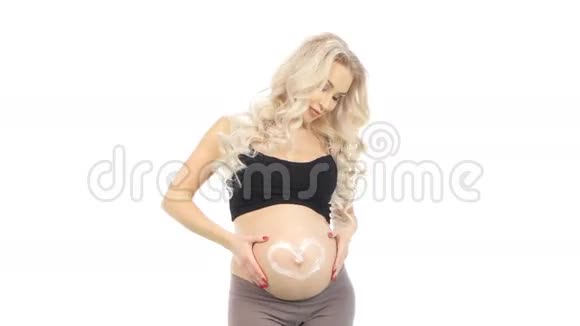 怀孕的金发碧眼的人会在她的腹部涂抹以心脏形式的奶油白色视频的预览图