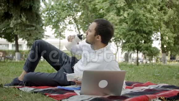 年轻的经理在公园里用笔记本电脑工作一边吃午饭视频的预览图