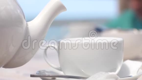 在海边的海滩咖啡馆里白色的茶壶慢慢地把茶倒进杯子里带着阳光3840x2160视频的预览图