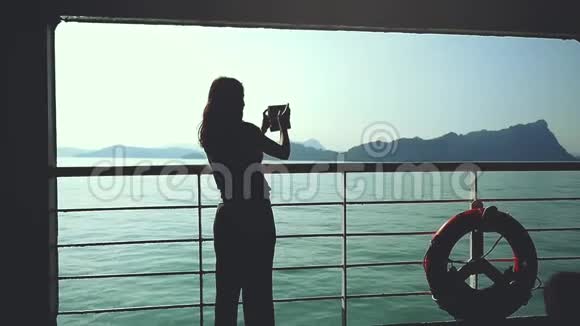 年轻的黑发女子站在游轮救生圈的甲板上用智能手机慢动作拍照视频的预览图