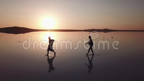 从无人机观察当人们在4K的背光下在日落时在粉红色的盐湖周围行走和奔跑时视频的预览图