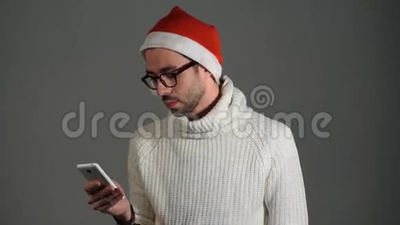 戴着眼镜戴着圣诞老人红帽的严肃残暴的男子通过电话打电话并对没有拨号感到愤怒视频的预览图