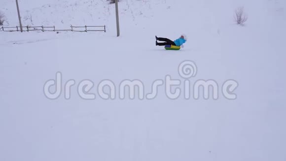 快乐的年轻女孩滑下雪滑到充气雪管上挥动她的手女孩在公园里玩视频的预览图