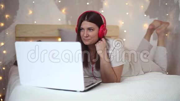 美丽的女孩用笔记本电脑听音乐心情很好躺在床上视频的预览图