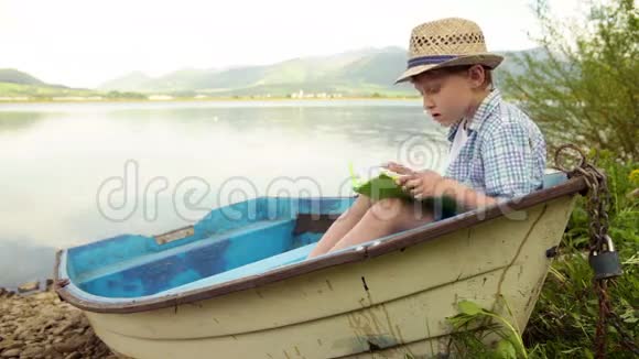 一个男孩坐在岸边的船上看书视频的预览图