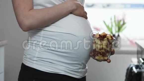 一个孕妇在拿着水果沙拉的时候抚摸她的腹部视频的预览图