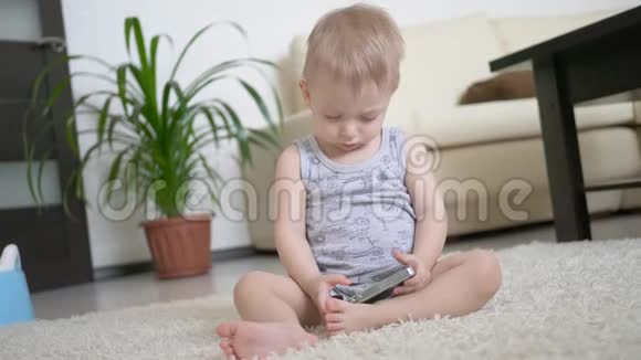 小男孩在家里的地板上看智能手机上的卡通生活方式视频的预览图