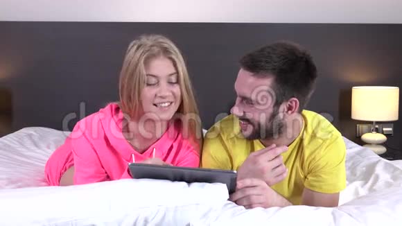 一对轻松的年轻夫妇在家里的床上使用数码平板电脑视频的预览图