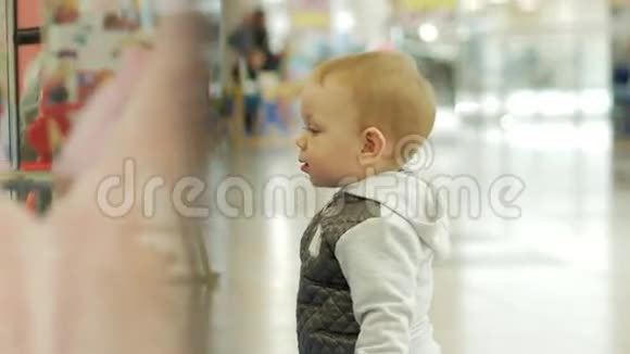 一个两岁的可爱金发男孩正在考虑通过玻璃开一家商店孩子仔细检查了里面视频的预览图