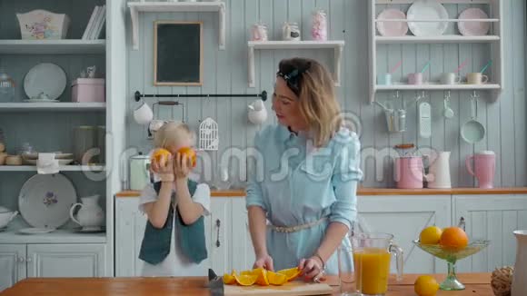 美丽快乐的妈妈带着橘子和果汁的孩子在厨房里微笑着玩水果视频的预览图