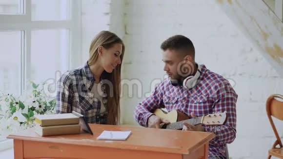 年轻快乐有爱心的一对夫妇在家坐在餐桌旁玩吉他玩得开心视频的预览图