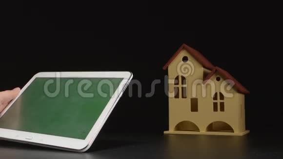 商人手中拿着一台平板电脑靠近一张桌子上的房子模型绿色屏幕视频的预览图