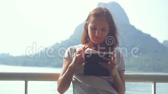 年轻的黑发女人站在游轮甲板上缓慢地使用她的智能手机1920x1080视频的预览图