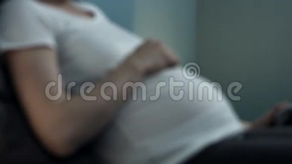 孕妇坐在床上拿着手机和耳机在胃里视频的预览图